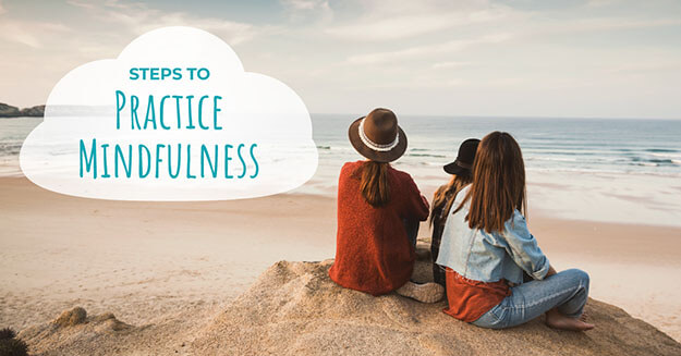 A group of people sitting on a beach looking out at the waves with the words steps to practice mindfulness.